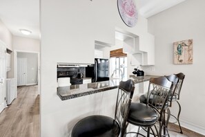Une cuisine moderne dotée d’un coin bar, d’appareils électroménagers en acier inoxydable et d’un espace détente avec des tabourets de bar.