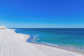 Ein Strand mit klarem Himmel, sandigem Ufer und Gebäuden im Hintergrund.