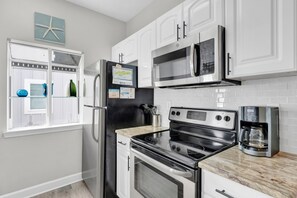A kitchen with white cabinets, a black refrigerator, a microwave, an oven, and a coffee maker. - Dolphin View Beachfront Duplex B | Pet Friendly (Gulf Shores)