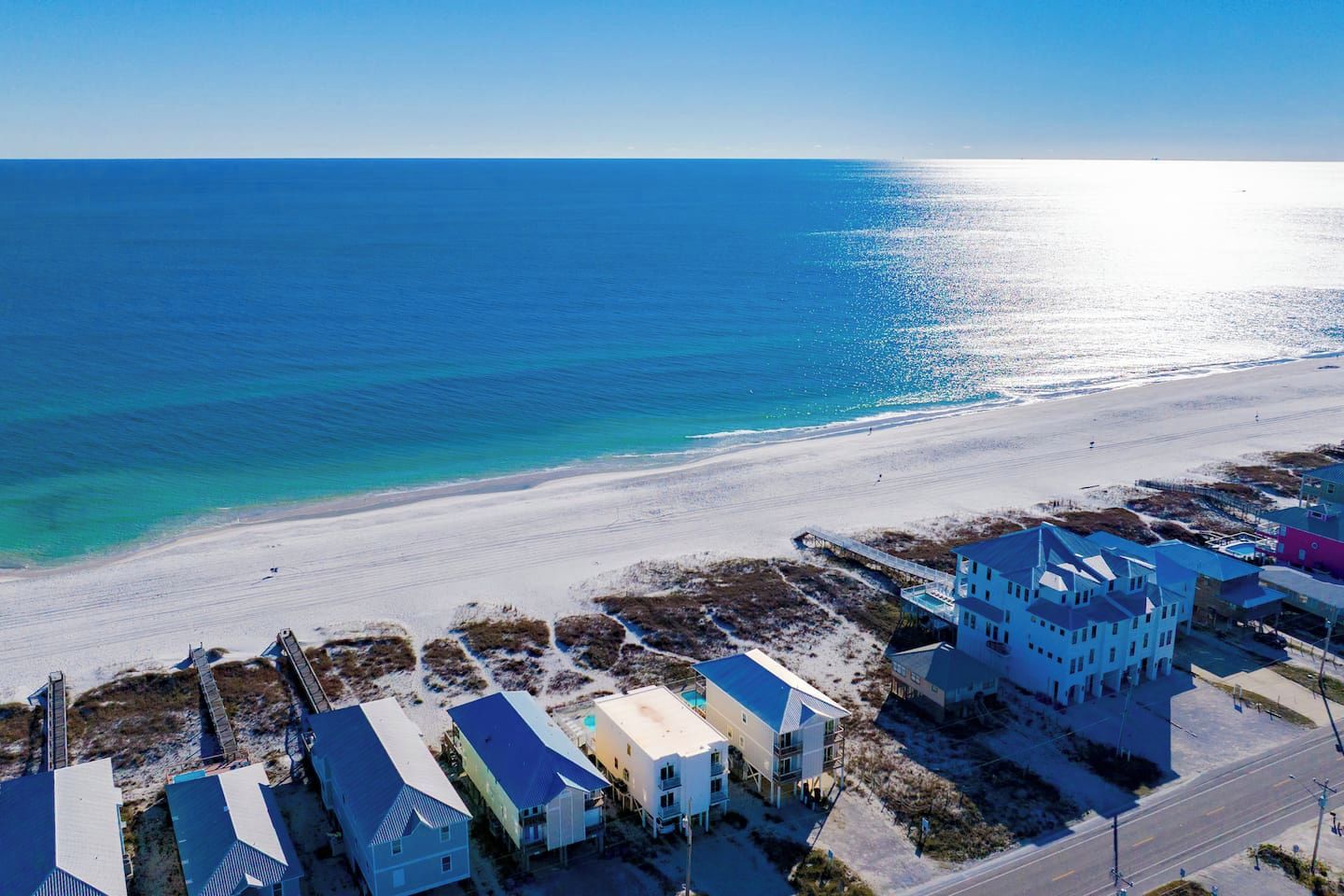 An aerial view of a coastal area with a beach, a pier, and buildings with a modern architectural style.