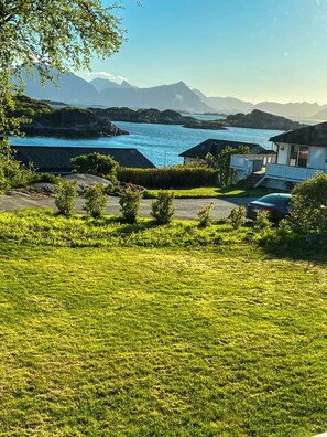 Une propriété située sur la côte, avec une pelouse verdoyante, une petite maison dotée d’un balcon et une vue sur la mer et les montagnes.