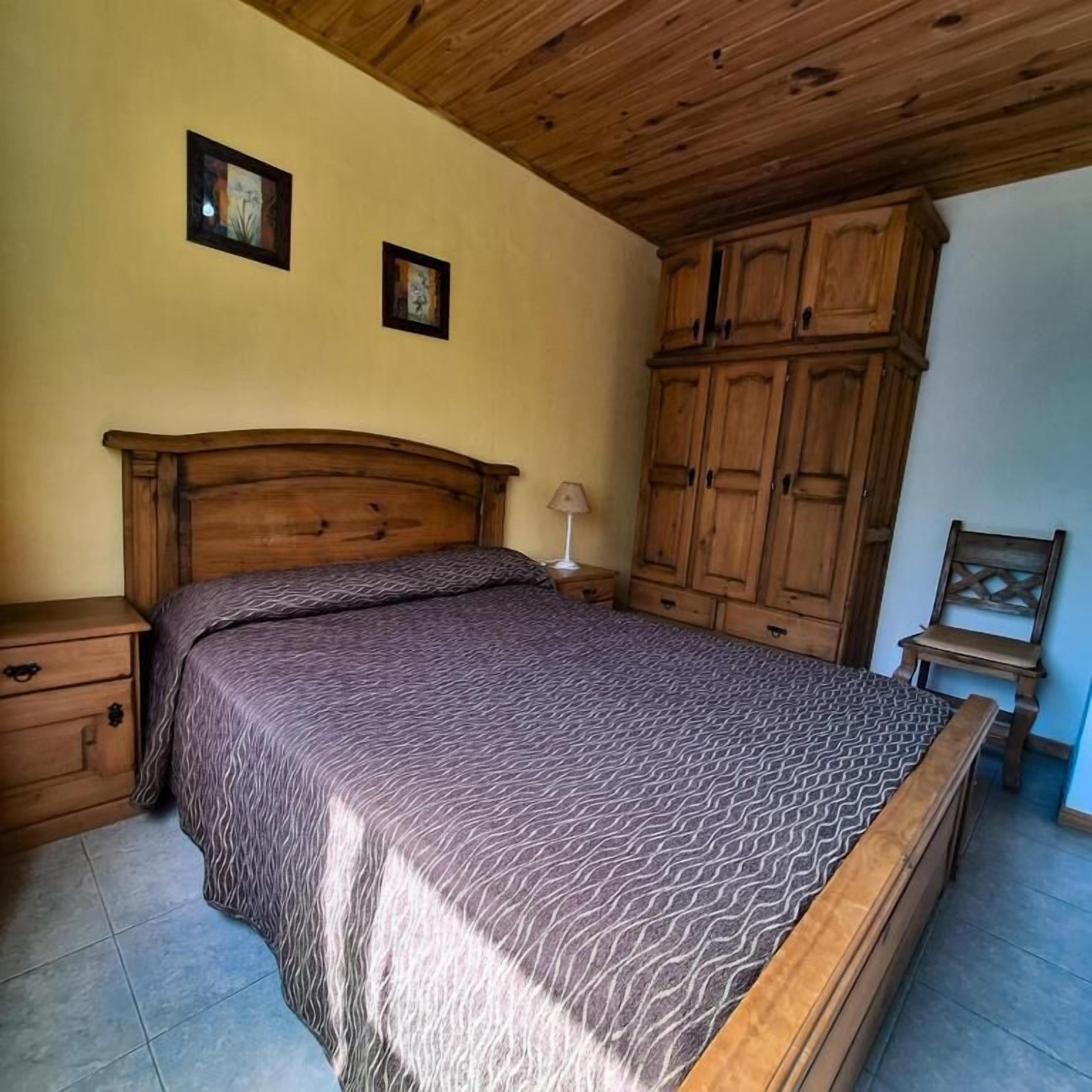 Een slaapkamer met een houten bed, nachtkastjes, een kledingkast en een stoel.