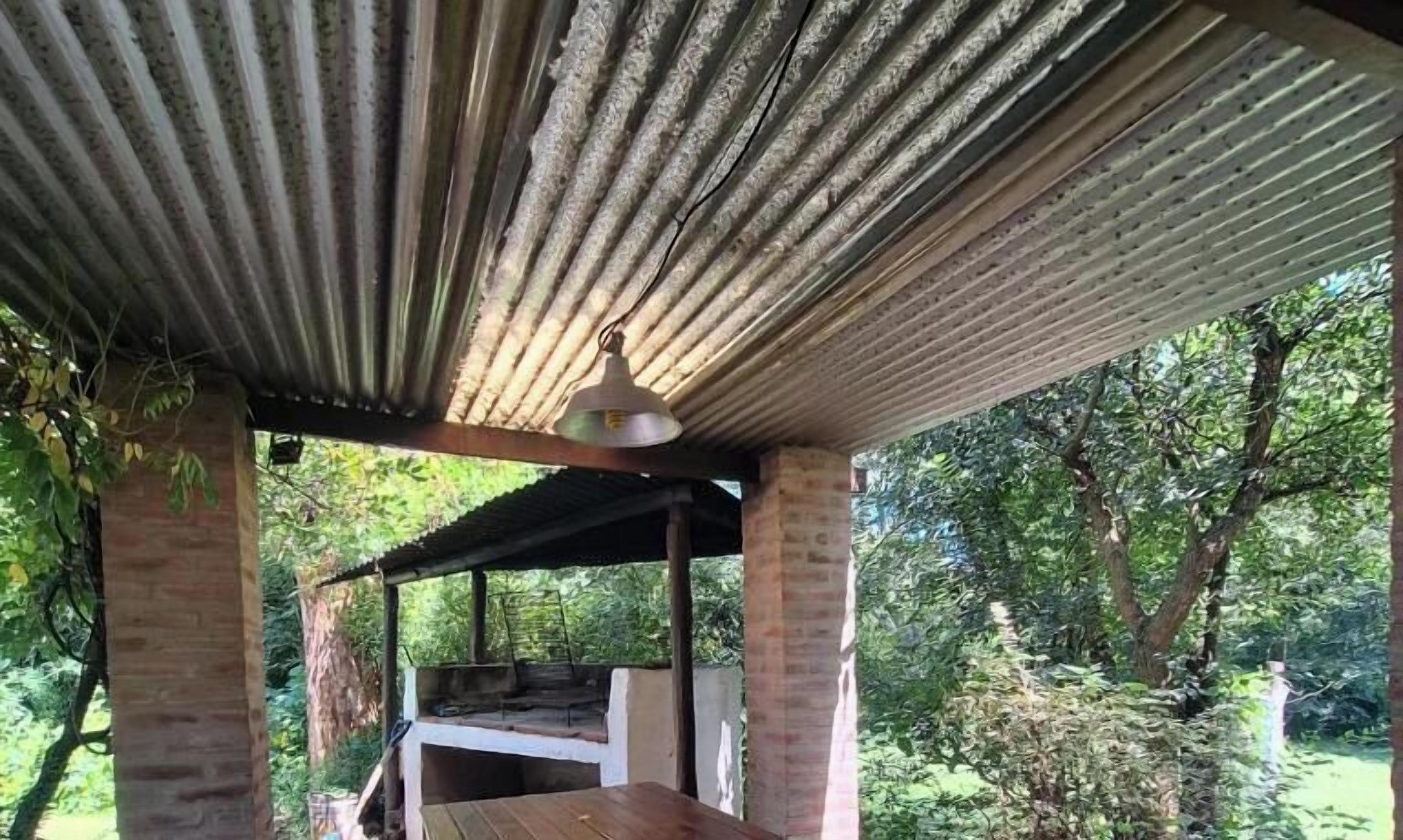 Un espace extérieur abrité, doté d’un banc en bois, d’un luminaire suspendu et offrant une vue sur une zone boisée.