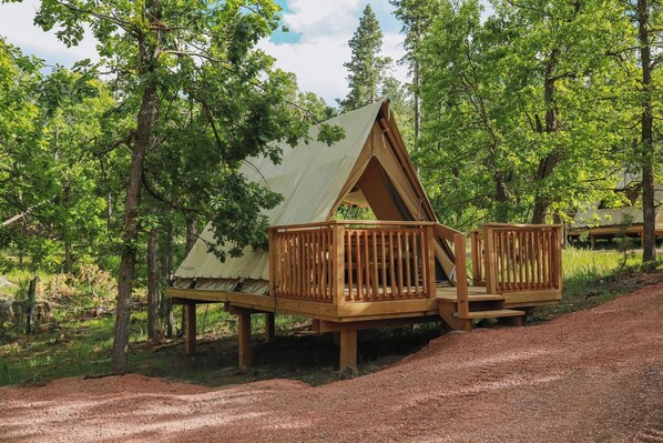 A wooden cabin with a triangular roof, a deck, and a covered seating area.