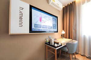Habitación de hotel con un televisor montado mostrando un anuncio de productos para el cuidado de la piel, un escritorio con una silla, una botella de agua y una lámpara.