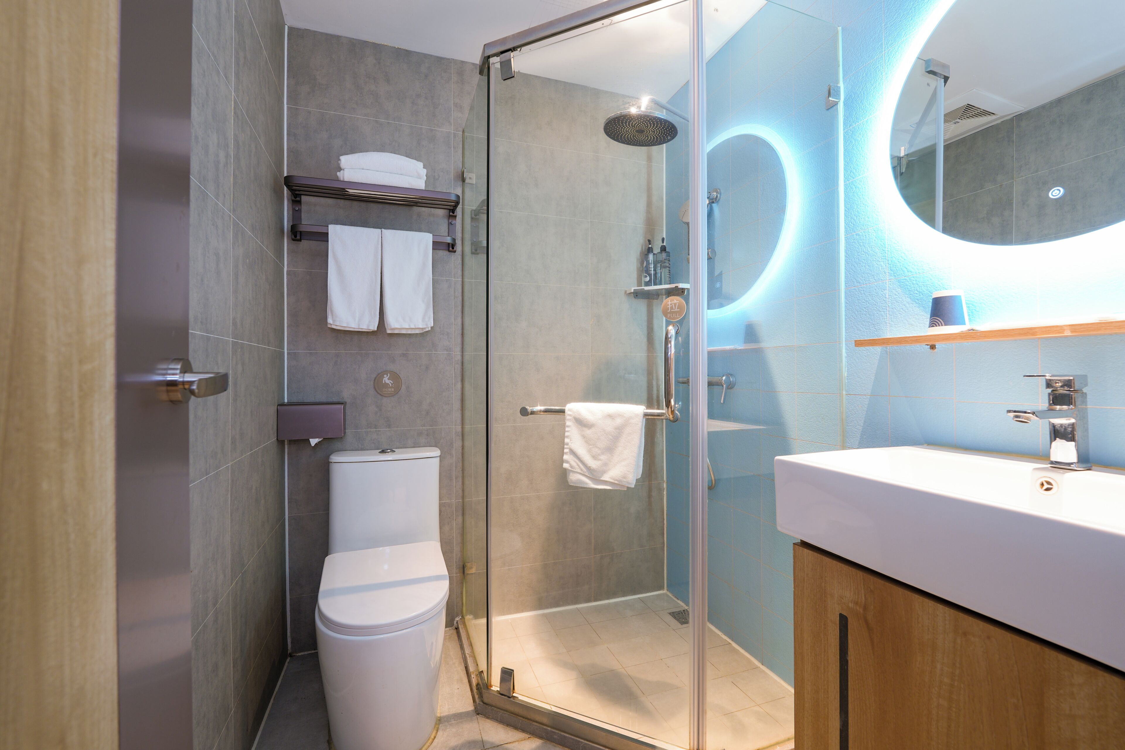 Une salle de bain moderne avec une douche à parois de verre, des toilettes blanches, un lavabo avec un miroir et un porte-serviettes.