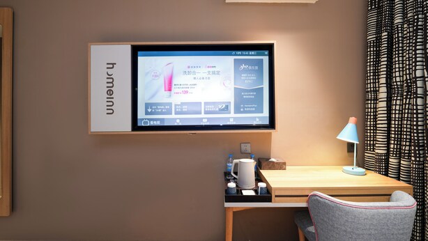 Habitación de hotel con televisor montado, escritorio con lámpara, silla y cafetera.