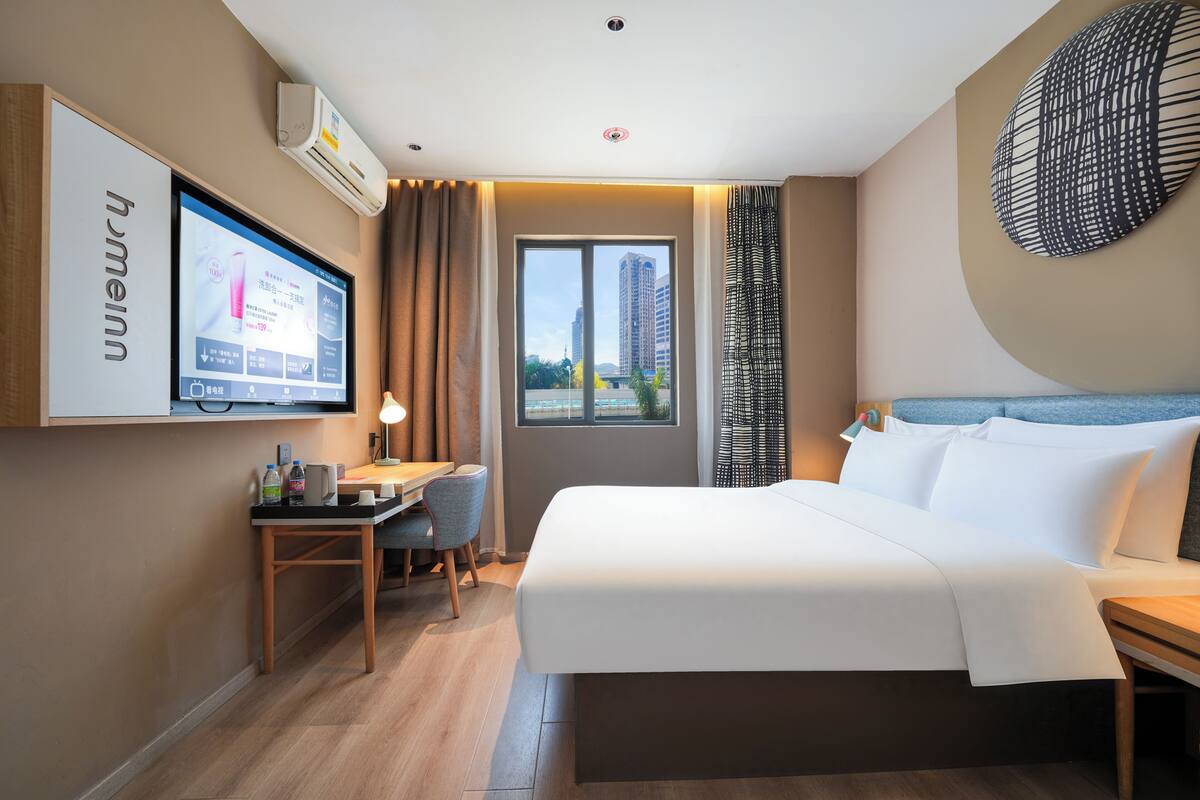 Una camera d'albergo con un letto, una scrivania, una sedia, una televisione e vista sugli edifici.