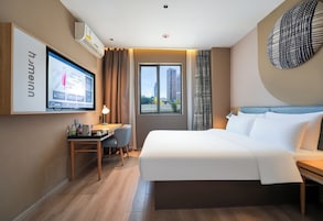 Habitación de hotel con cama, escritorio, silla, televisor y vistas a edificios.