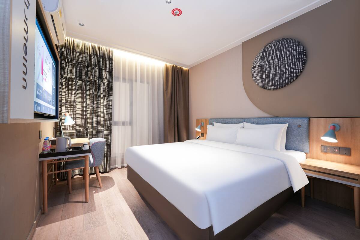 Camera d'albergo con un letto, una scrivania, una sedia, una TV e tende.