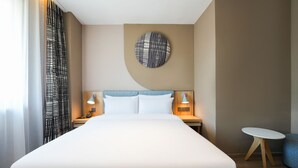 Habitación de hotel con una cama grande, dos mesitas de noche con lámparas, un adorno redondo en la pared y una pequeña mesa redonda.