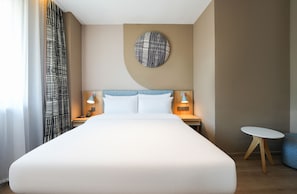 Habitación de hotel con una cama grande, dos mesitas de noche con lámparas, un adorno redondo en la pared y una pequeña mesa redonda.