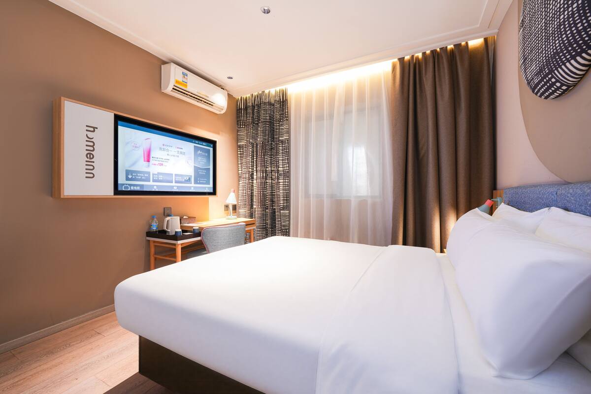 Una camera d'albergo con un letto, una scrivania con un computer, un condizionatore d'aria e una TV a parete.