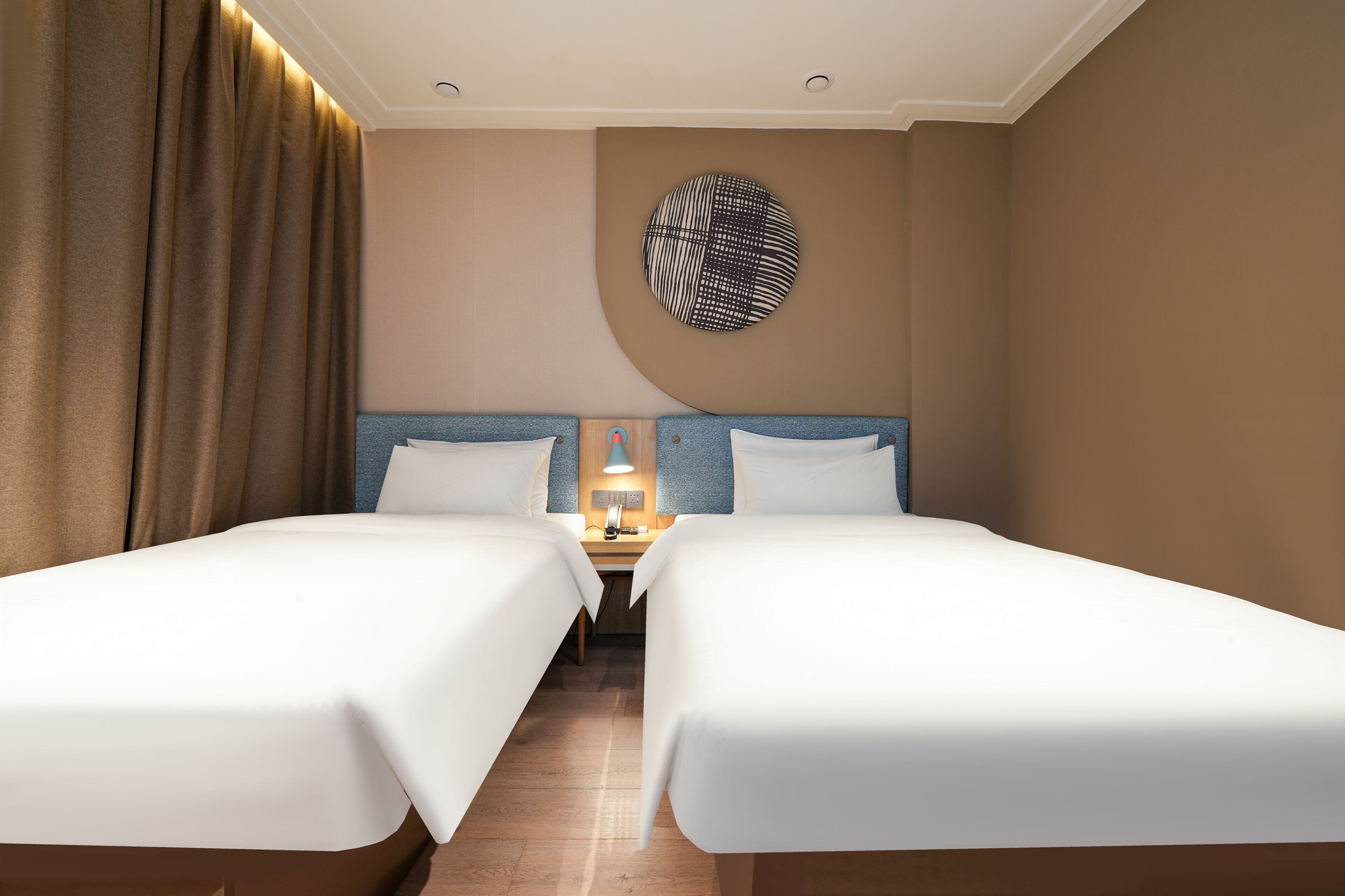 A hotel room with two beds, a nightstand, a lamp, and a circular wall decoration.