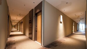 Un largo y estrecho pasillo de hotel con puertas a ambos lados, pisos alfombrados e iluminación empotrada.