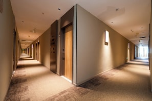 Un largo y estrecho pasillo de hotel con puertas a ambos lados, pisos alfombrados e iluminación empotrada.