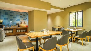 Un restaurante con varias mesas y sillas, una barra con productos alimenticios y un amplio ventanal que proporciona luz natural.