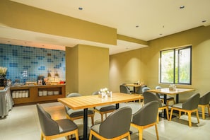 Un restaurante con varias mesas y sillas, una barra con productos alimenticios y un amplio ventanal que proporciona luz natural.