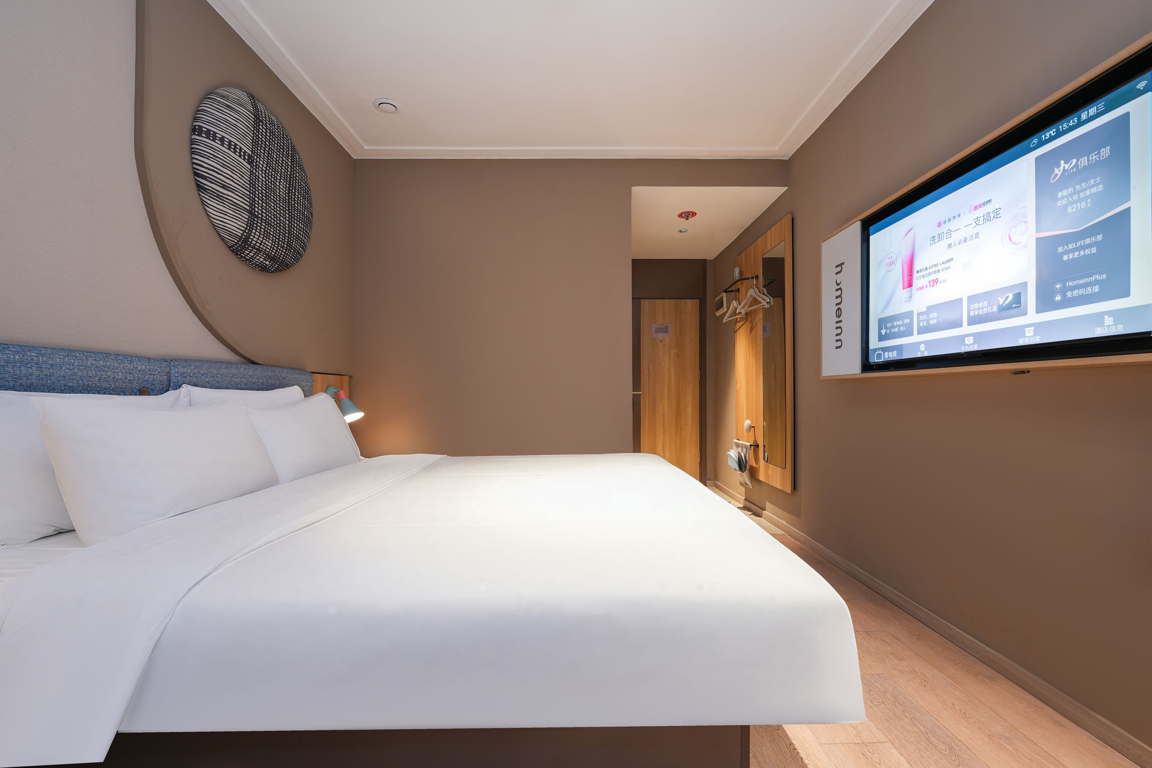 A hotel room with a bed, a TV mounted on the wall, and a wooden door.