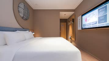 A hotel room with a bed, a TV mounted on the wall, and a wooden door.
