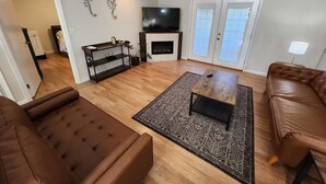 Een woonkamer met een bruine leren bank, een salontafel, een televisie, een open haard en een kamerbreed tapijt met dessin.