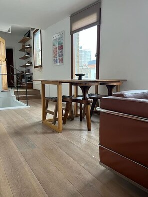 A modern living room with a wooden dining table, a brown sofa, and a staircase leading to an upper floor. - Modern East London (terrace) (Greater London)