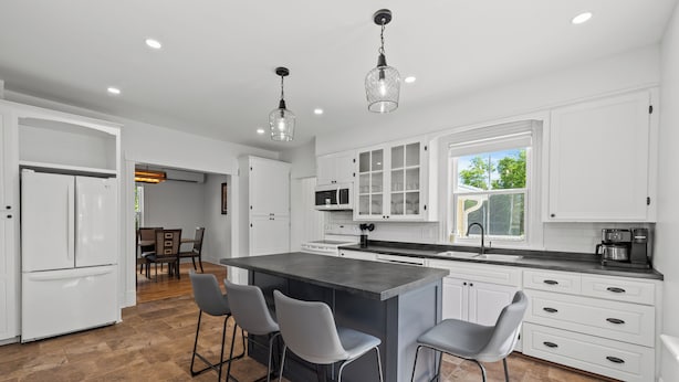 A modern kitchen with white cabinetry, a central island with bar stools, and pendant lighting. - Cavendish Gables Cottage (Green Gables)