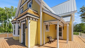 A yellow building with a covered porch and a wooden deck. - Cavendish Gables Cottage (Green Gables)