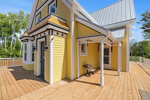 A yellow building with a covered porch and a wooden deck. - Cavendish Gables Cottage (Green Gables)