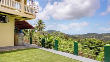 A building with a balcony, a green fence, and a view of mountains.