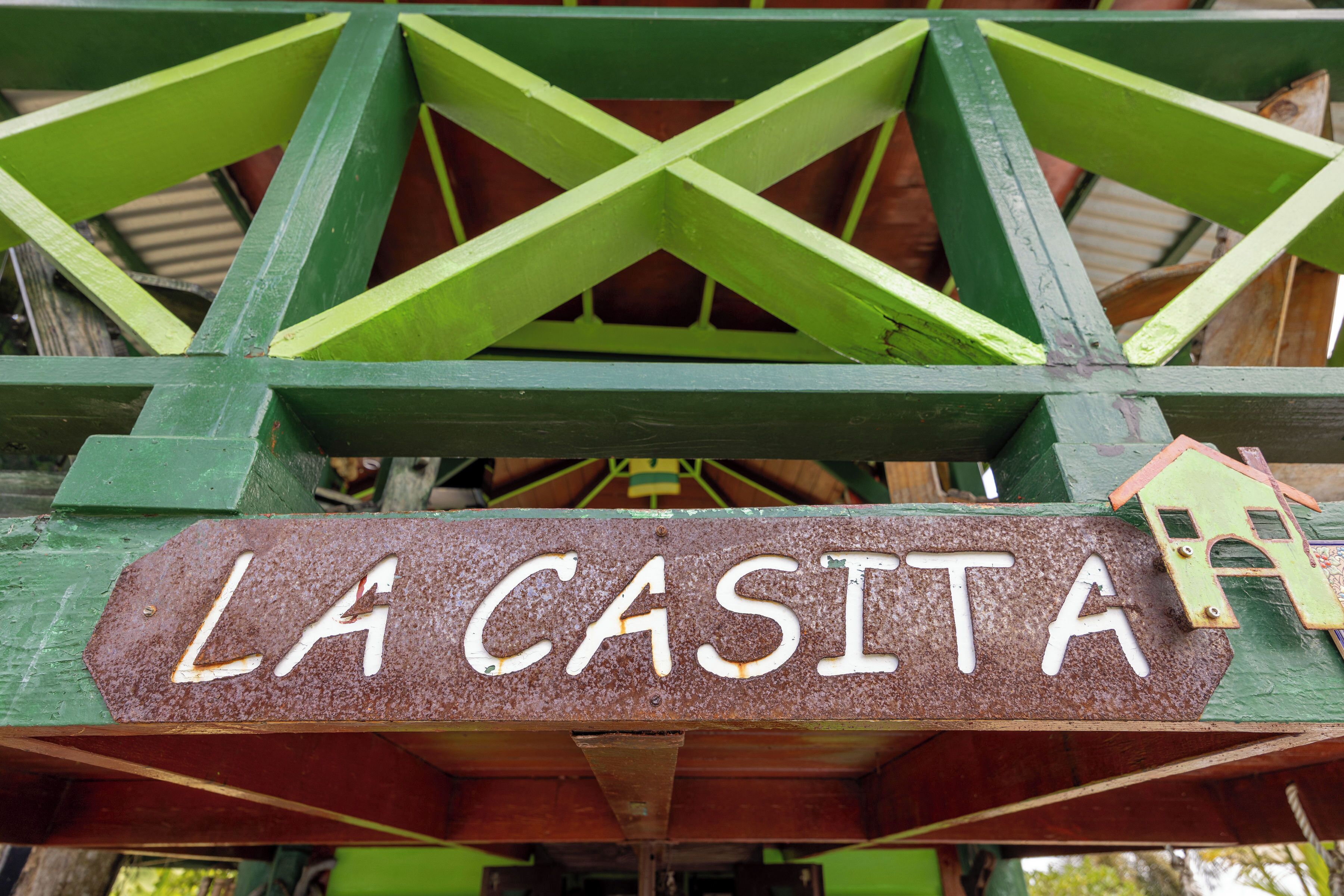 Een bord met de tekst 'LA CASITA', bevestigd aan een constructie met groene balken.