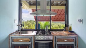 Une cuisine compacte équipée d’une cuisinière à gaz, d’un four encastré et d’une fenêtre donnant sur un espace verdoyant.
