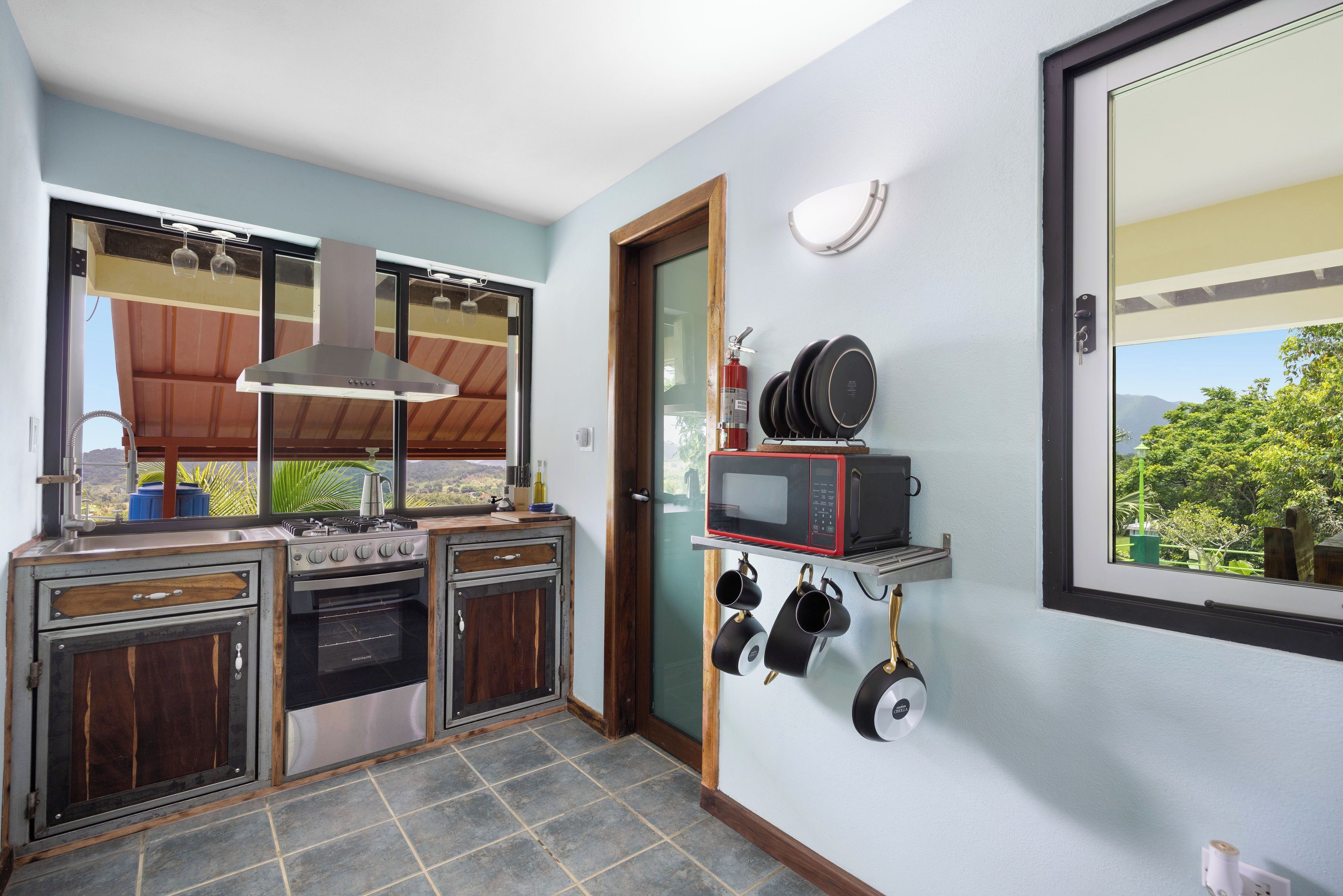 Una cocina con estufa, horno y microondas, una ventana con vistas, y una puerta con extintor.
