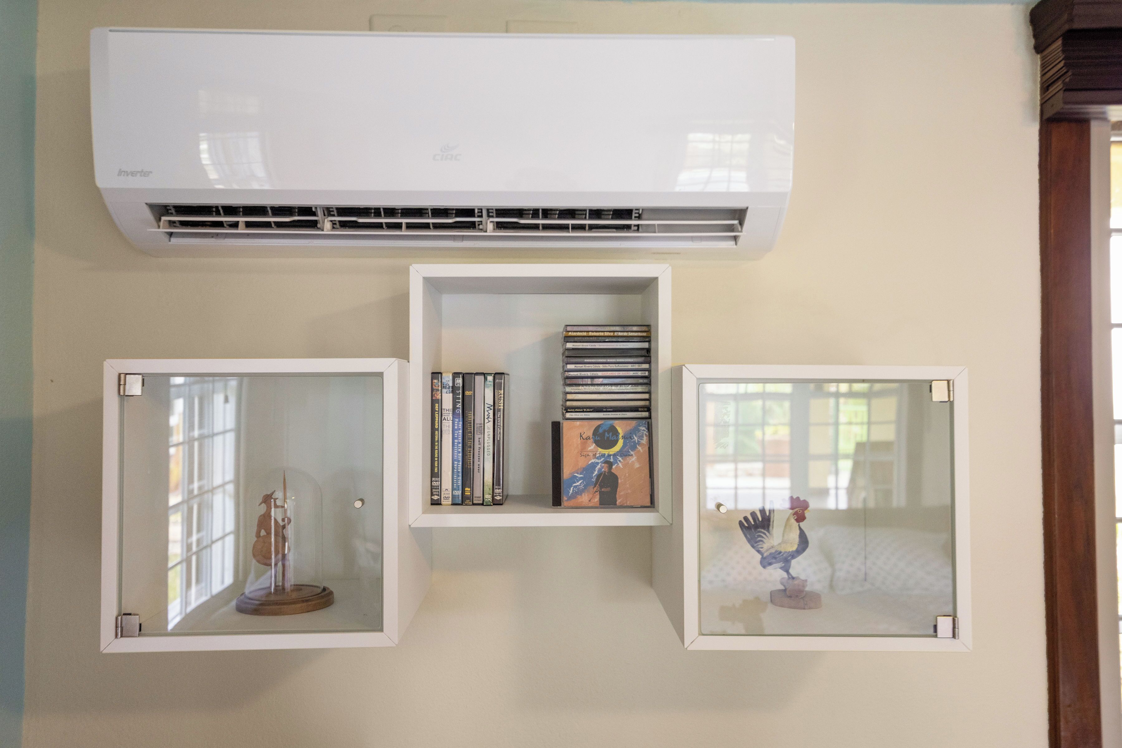 A wall-mounted air conditioner, a glass display case with a figurine, and a shelf with books and a decorative item.