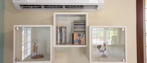 A wall-mounted air conditioner, a glass display case with a figurine, and a shelf with books and a decorative item.