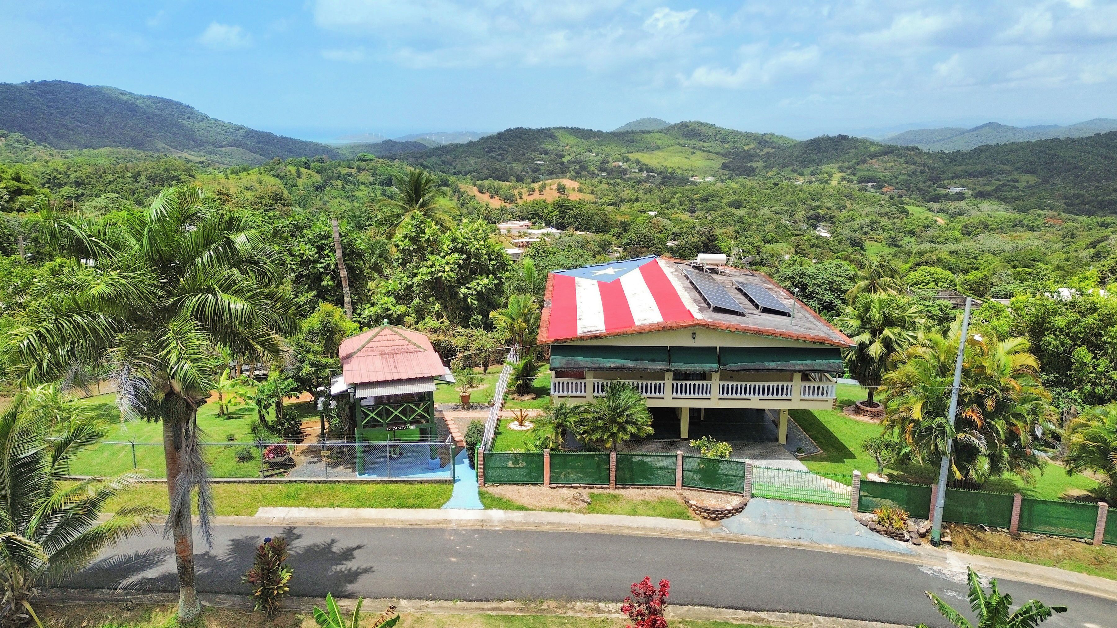 A hotel with a red and white striped roof, surrounded by lush greenery and hills.
