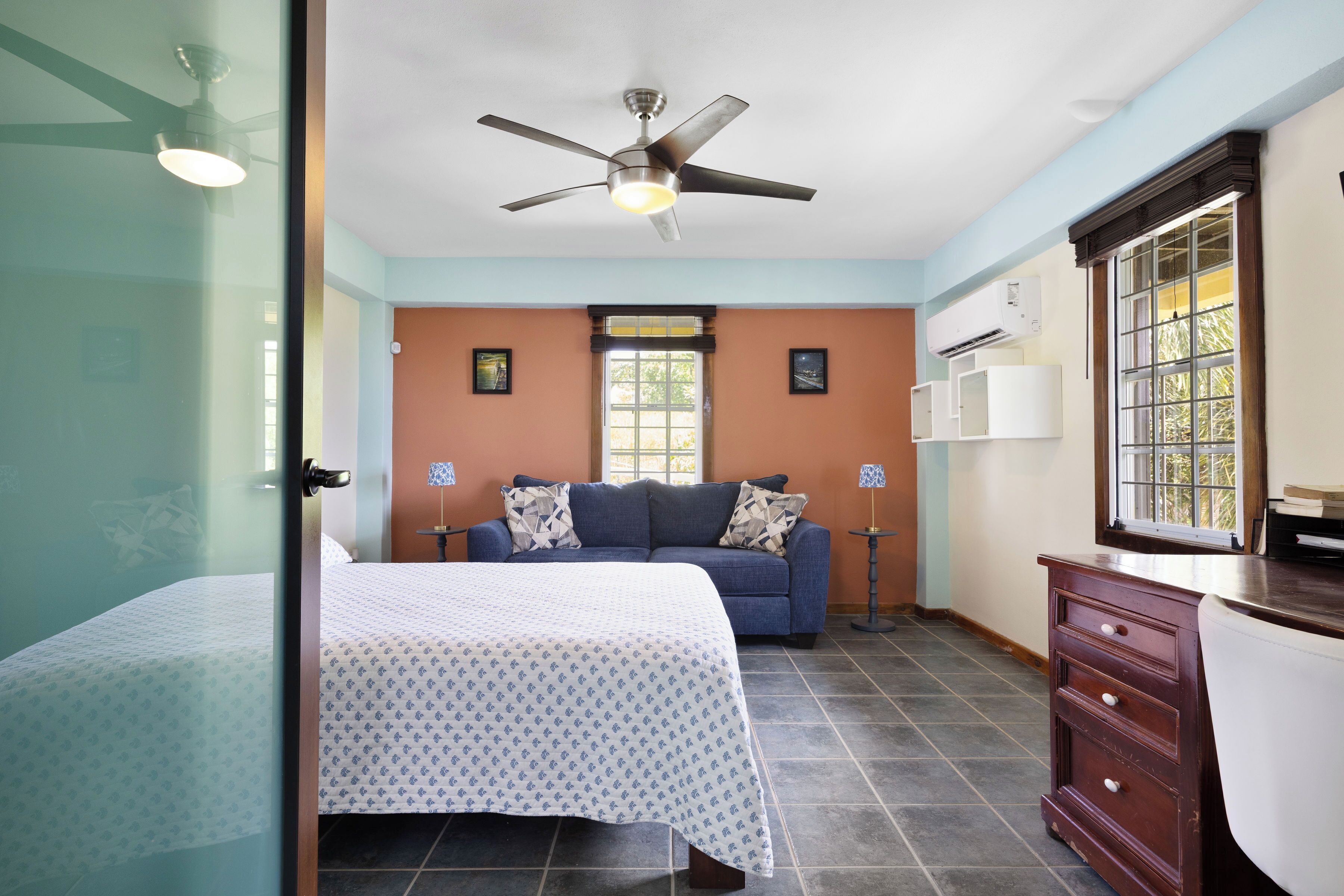 Un dormitorio con cama, sofá azul, cómoda y ventilador de techo.