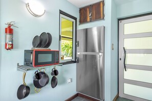 Uma cozinha com geladeira de aço inoxidável, micro-ondas e panelas penduradas.