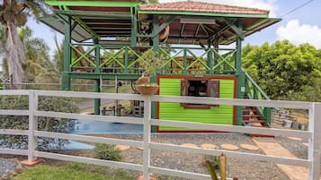 A green and red structure with a small window and a door, surrounded by a white fence.