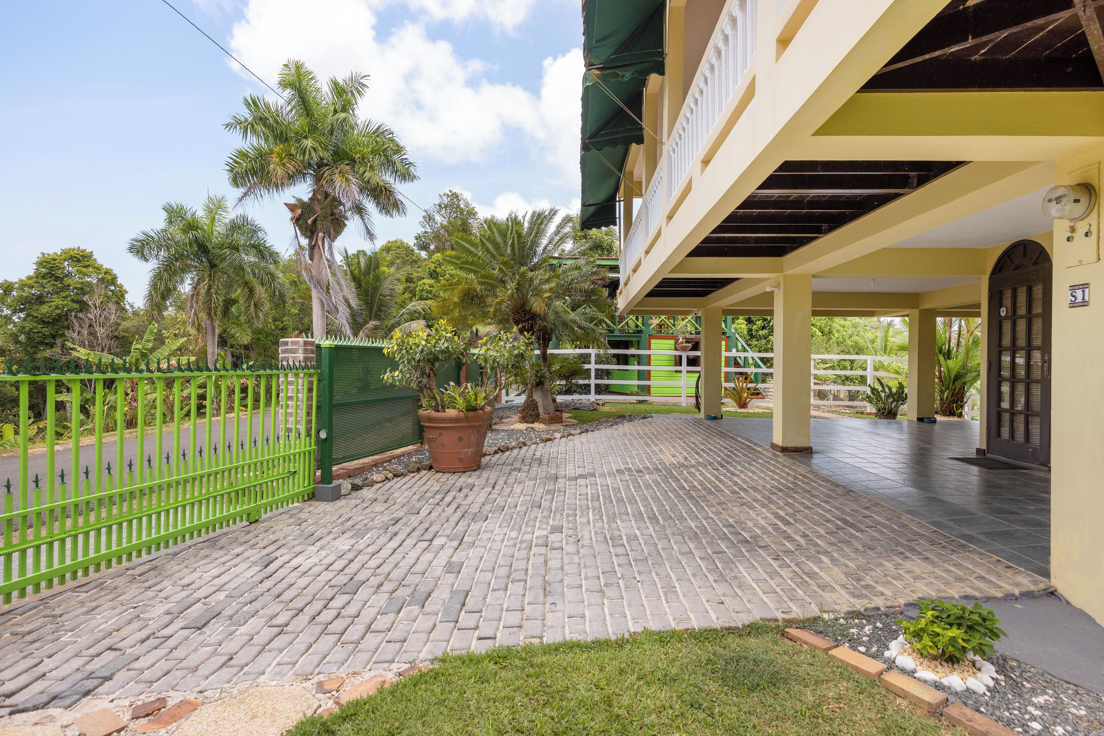Un patio empedrado con cercado verde, plantas en macetas y un edificio con balcón.