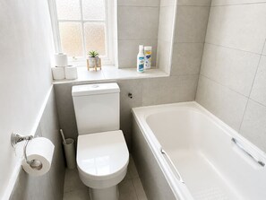 A bathroom with a toilet, a bathtub, and a window with a plant. - 2-Bedroom Home with FREE Parking near Sydenham Station (Greater London)