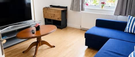 A living room with a television, a wooden coffee table, a blue sofa, and a window with curtains.
