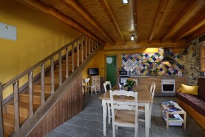 A wooden staircase leading to a dining area with a table and chairs, a kitchen with a stone wall, and a green door. - The LLananzanes Lookout - Rural Asturias - HOUSE I (Conforcos (Aller))