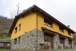 A two-story building with a yellow facade and stone foundation, featuring a porch with outdoor seating. - The LLananzanes Lookout - Rural Asturias - HOUSE I (Conforcos (Aller))
