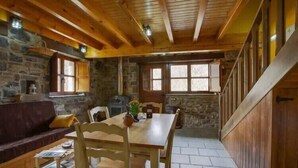 A rustic cabin interior with a stone wall, wooden beams, a dining table, and a fireplace. - The LLananzanes Lookout—Asturias Rural—CASA II (Conforcos (Aller))