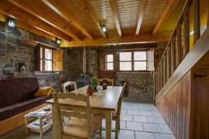 Ein rustikales Blockhaus-Interieur mit Steinwand, Holzbalken, einem Esstisch und einem Kamin.