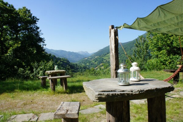 Eine rustikale Außenanlage mit einem Steintisch, zwei Laternen und einem grünen Blätterdach.