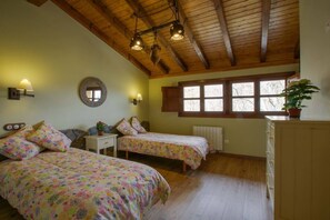 Ein Schlafzimmer mit zwei Betten, Holzbalkendecke, einem Fenster mit Fensterläden und einer Topfpflanze.