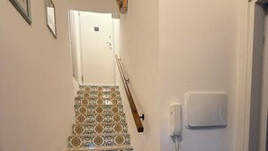 Eine Treppe mit gemusterten Fliesen führt zu einer Tür mit Lichtschalter und Wandleuchte.