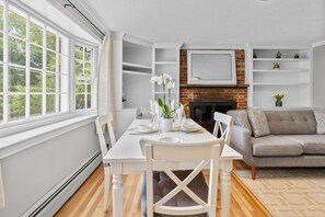 A dining area with a table set for two, a sofa, and a fireplace. - Cozy 2BR Family Home with Fire Pit and Backyard (Barnstable)